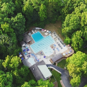 Peakland Pool in Lynchburg, VA. A birds-eye view of the 25 Meter Pool, High dive diving boards, baby pool, relaxing seating area, and concession stand.